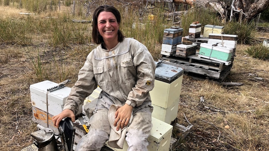 A fully kitted female beekeeper smiling at the camera near her hives in the Derwent Valley in Tasmania