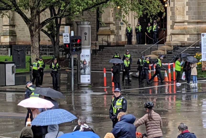 Police officers stand in the rain on the road and footpath waiting for protesters to arrive.