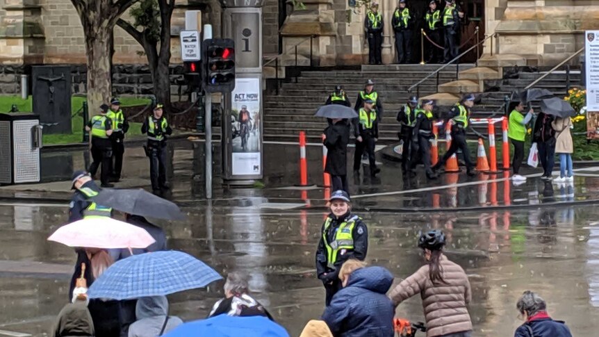 Police officers stand in the rain on the road and footpath waiting for protesters to arrive.