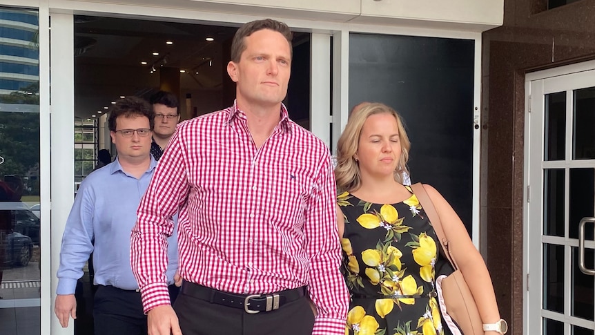 A group of people leave a courthouse. A man and a woman holding hands are at the front of the group.