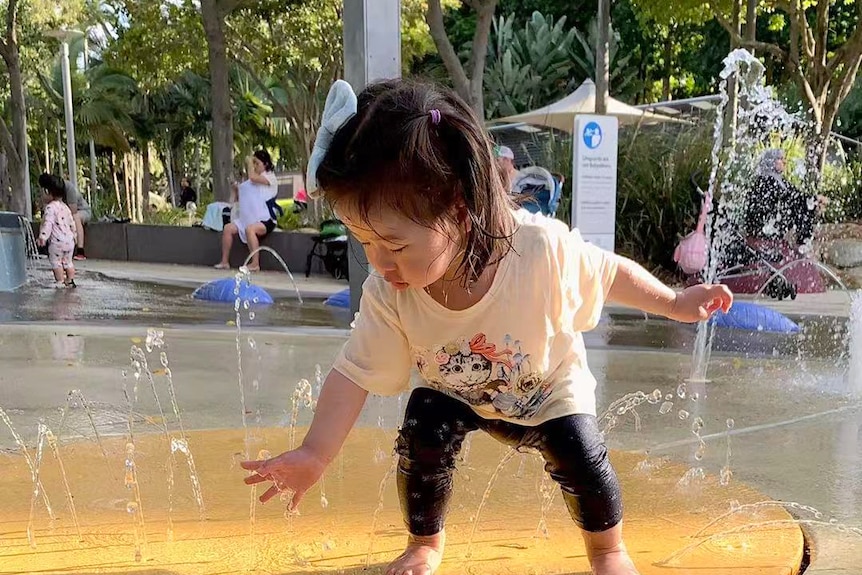 A toddler playing with water at an outdoor fountain.