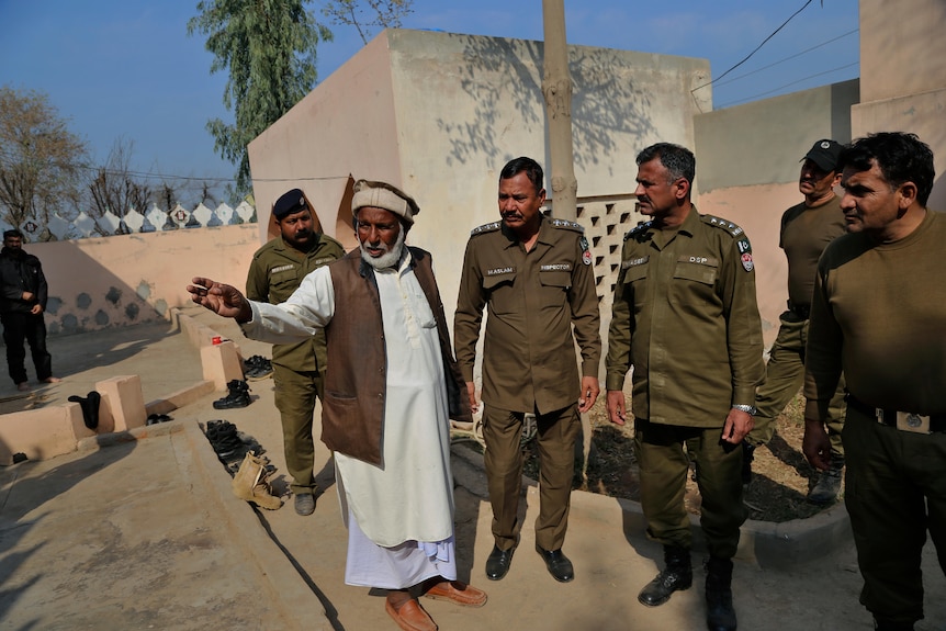 A mosque worker shows uniformed police around the courtyard of a mosque.