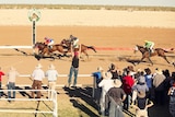An excited crowd watches the thrilling conclusion of an outback horse race.