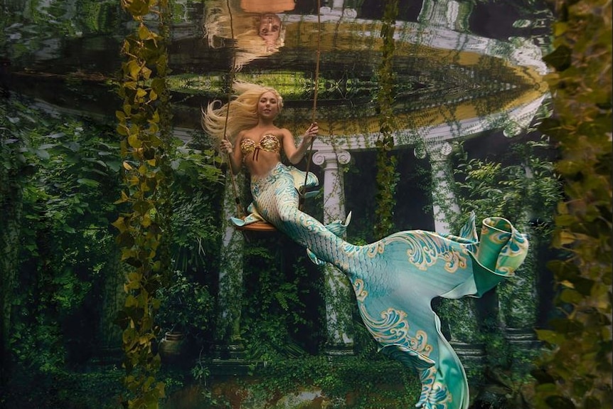 A woman in a mermaid costume on an underwater swing.