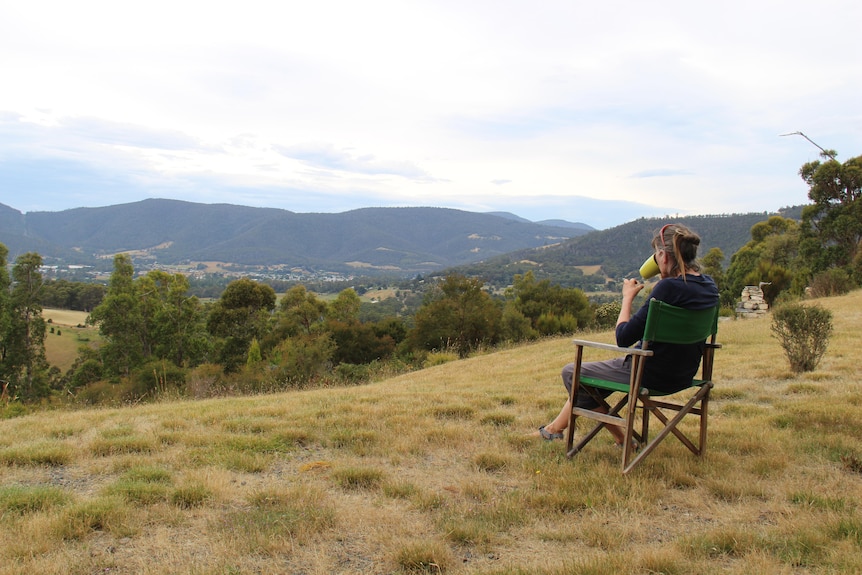 A woman sits on a camp chair on a hill and looks out over a valley.