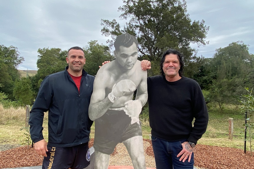 two men stand next to image of boxer