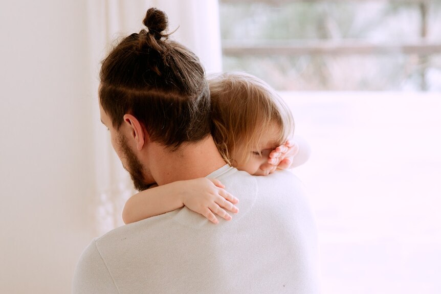 A man with his hair tied in a bun holds a baby