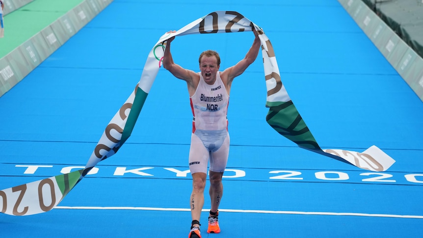 Norway's Kristian Blummenfelt at the finish line grabbing the tape and raising his arms in the air. 