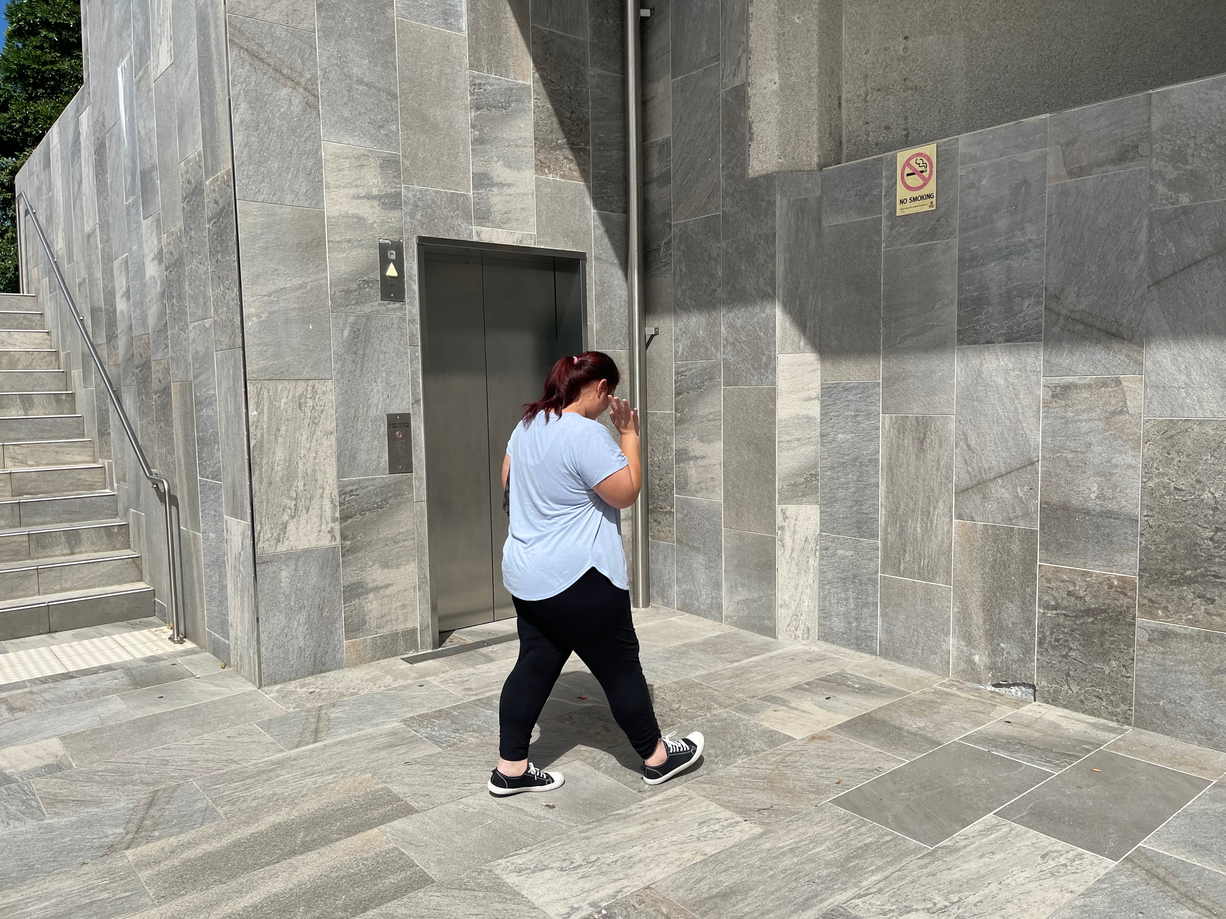 Una mujer se aleja de la cámara y se dirige a un ascensor.