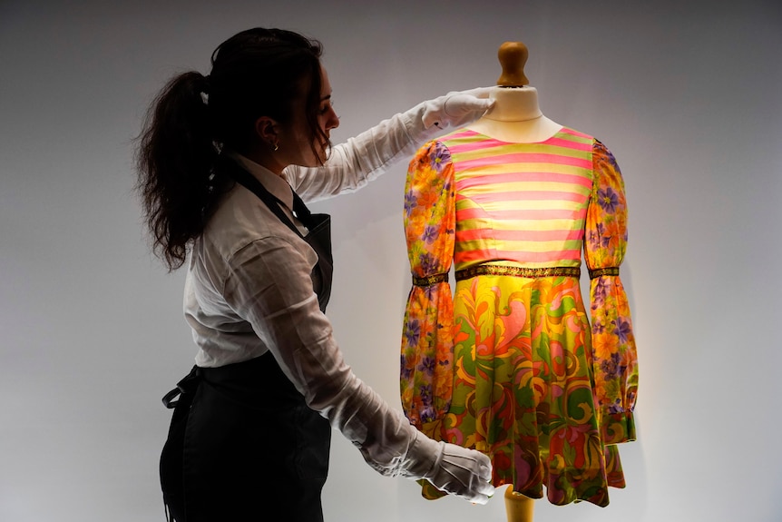 An auctioneer holds up a 1960s style dress 