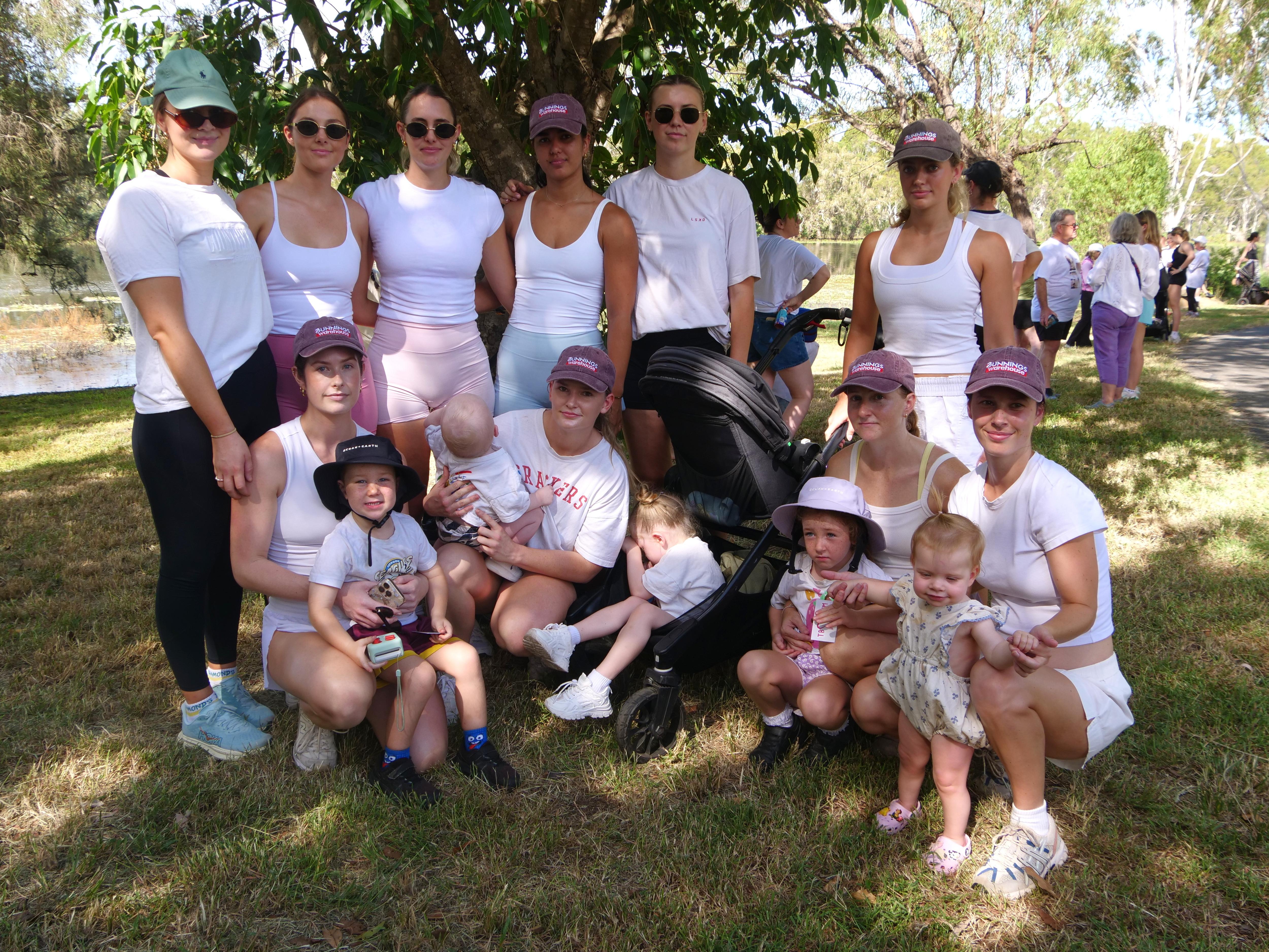 Grupo de 10 mujeres, algunas con niños pequeños, en ropa deportiva, todas con camisetas blancas.