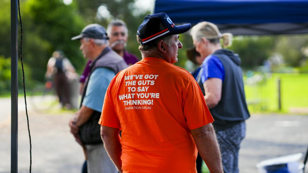 A man in a navy cap wears a bright orange shirt with the words  "We've got the guts to say what you're thinking" on the back.