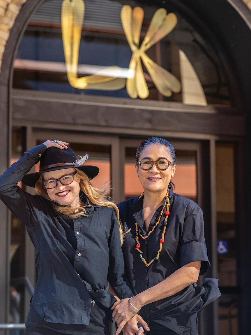 Two women smile standing outside a restaurant that has the initials LK at the entrance