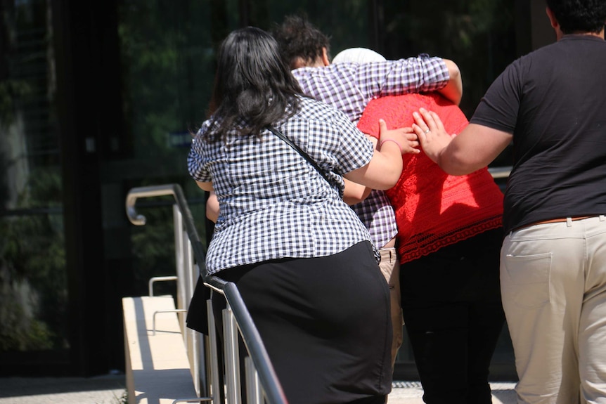 The catfish is surrounded by her family outside court, arms around her shoulders and supportive hands on her back.