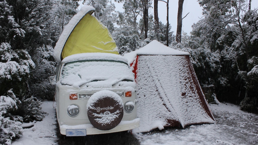A cream kombi van set up for camping in the snow.