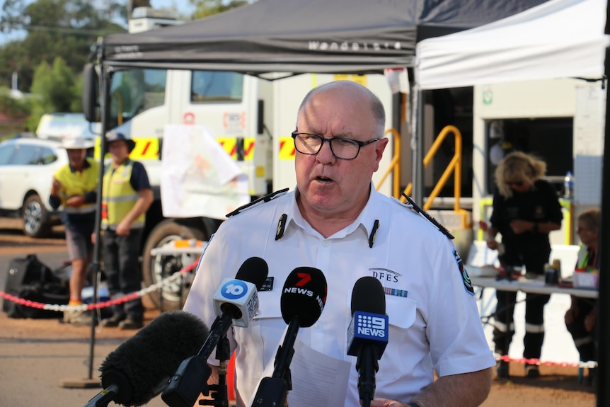 A middle-aged man in a uniform stands outdoors, speaking to the media.