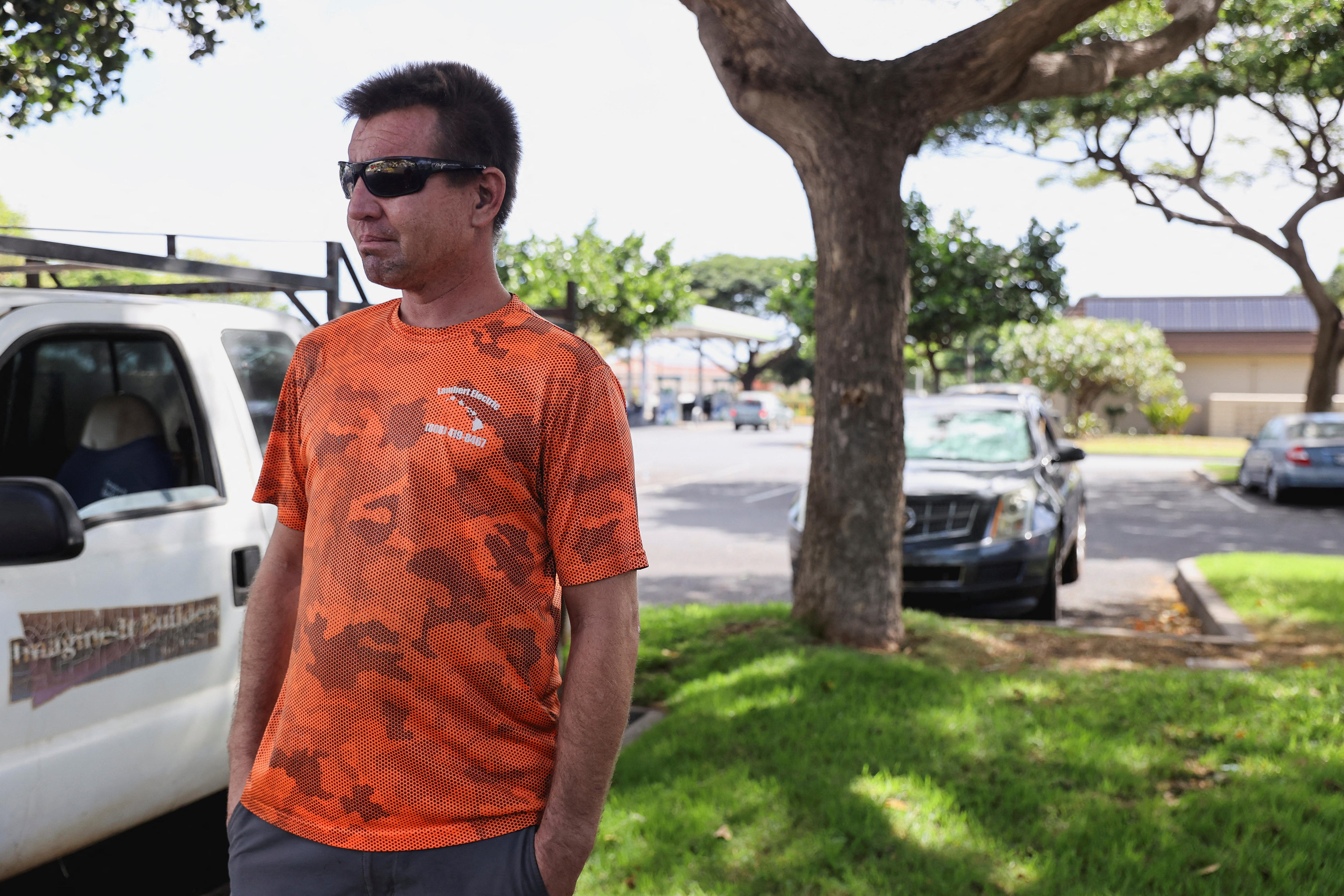 A man in an orange t shirt and sunglasses looks out at damage 
