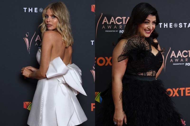 A blonde woman in a white structured dress and a dark-haired woman in a black gauzy dress pose on the red carpet.