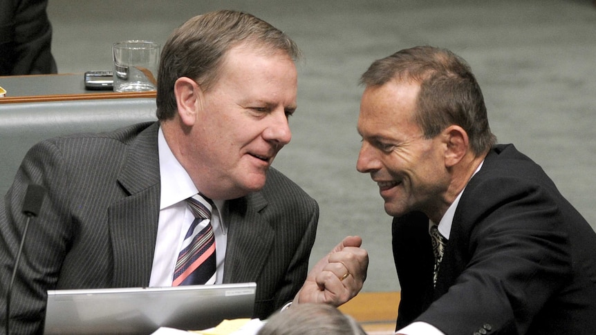 Tony Abbott smiles as he leans in to speak to Peter Costello