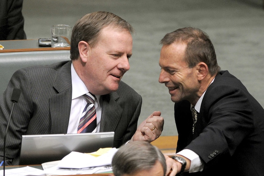 Tony Abbott smiles as he leans in to speak to Peter Costello