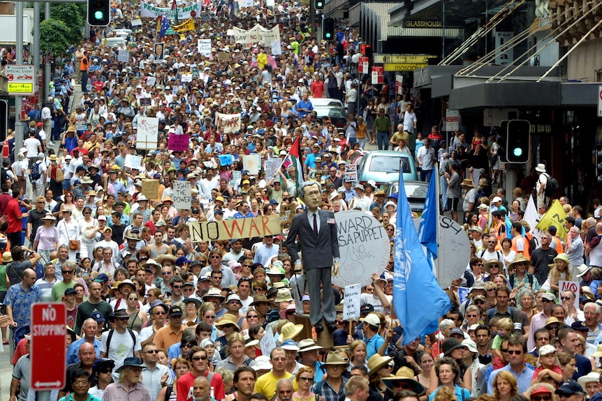 Wide angle photo shows a city street crammed with people holding anti-war signs and flags