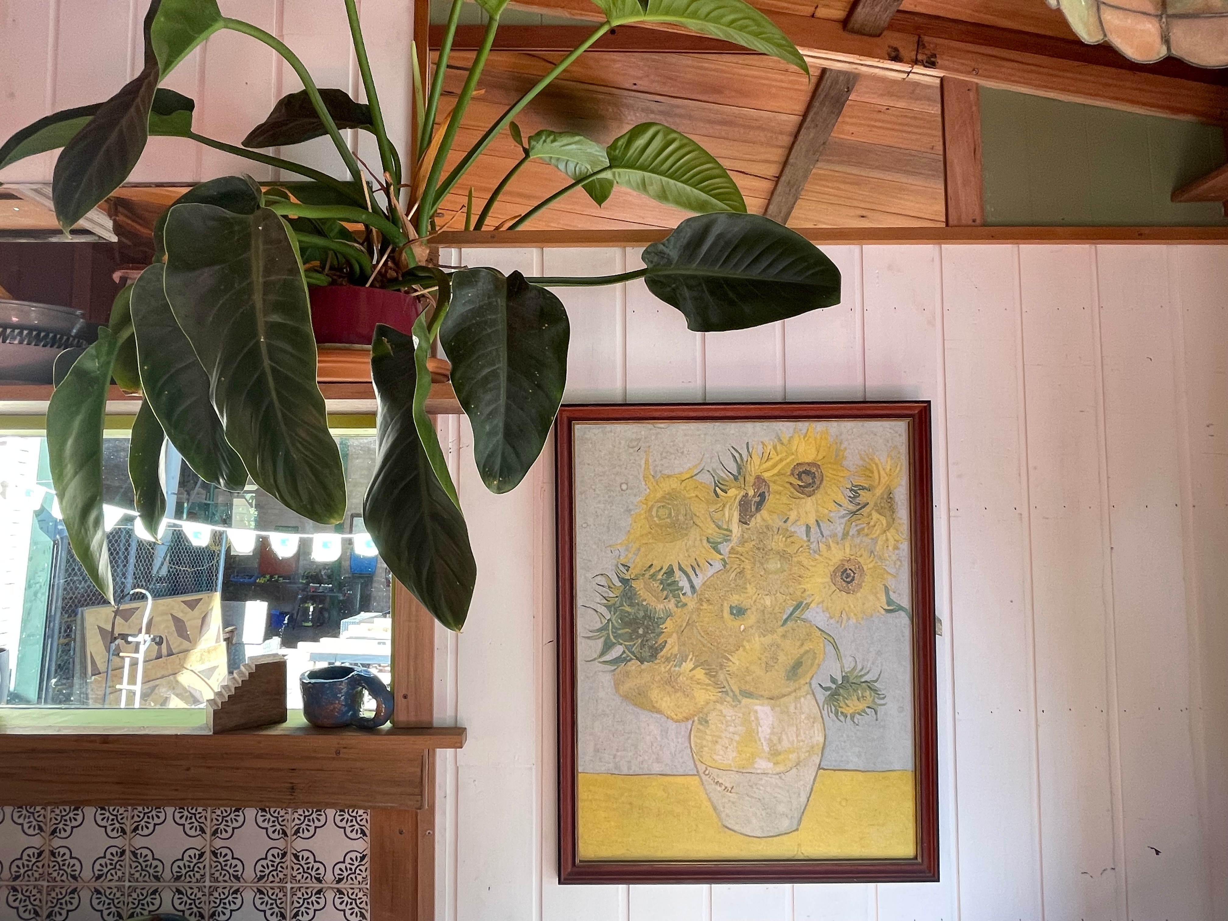 A framed print of Vincent Van Gogh's Sunflowers and a plant in a tiny home.
