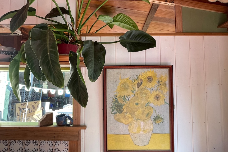 A framed print of Vincent Van Gogh's Sunflowers and a plant in a tiny home.