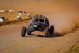Four-wheel drive car with big wheels races down a dirt road with dust flying out the back