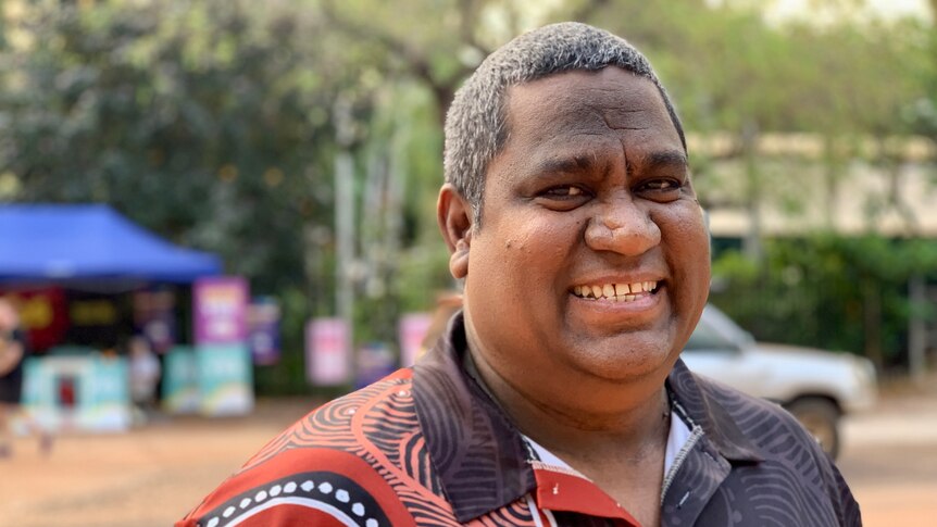 Headshot of a smiling Indigenous man in a patterned shirt