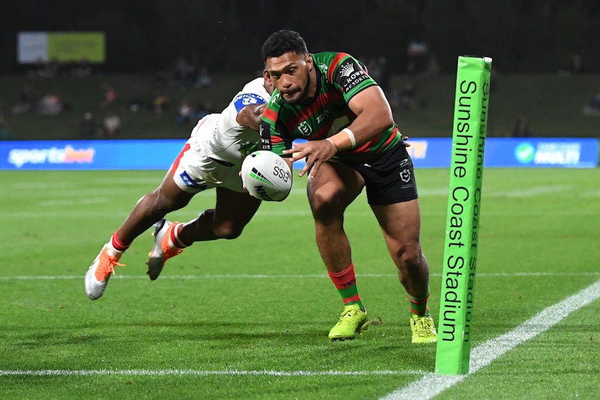 A South Sydney NRL player holds the ball in his right hand as he prepares to score a try.