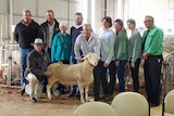 a group of people stand around a white ram in a shed