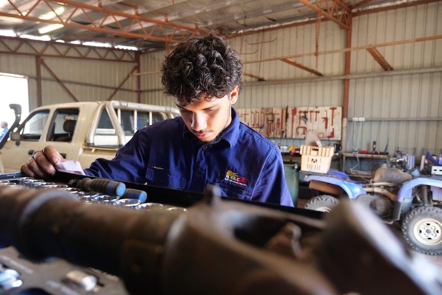 A young Indigenous man works on a car in a workshop