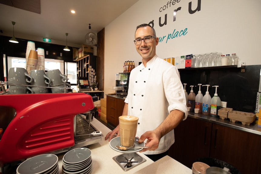 A man serves coffee from behind a machine in a cafe