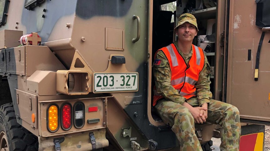 A man in army clothing sitting in the back of an Australian Defence Force truck.