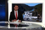 Bourchier at news desk with plasma screen showing ACT ABC News with Ngunnawal Country written underneath.