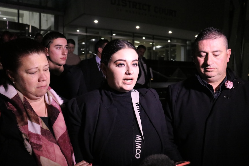 A sad looking lady addresses media in the dark outside court