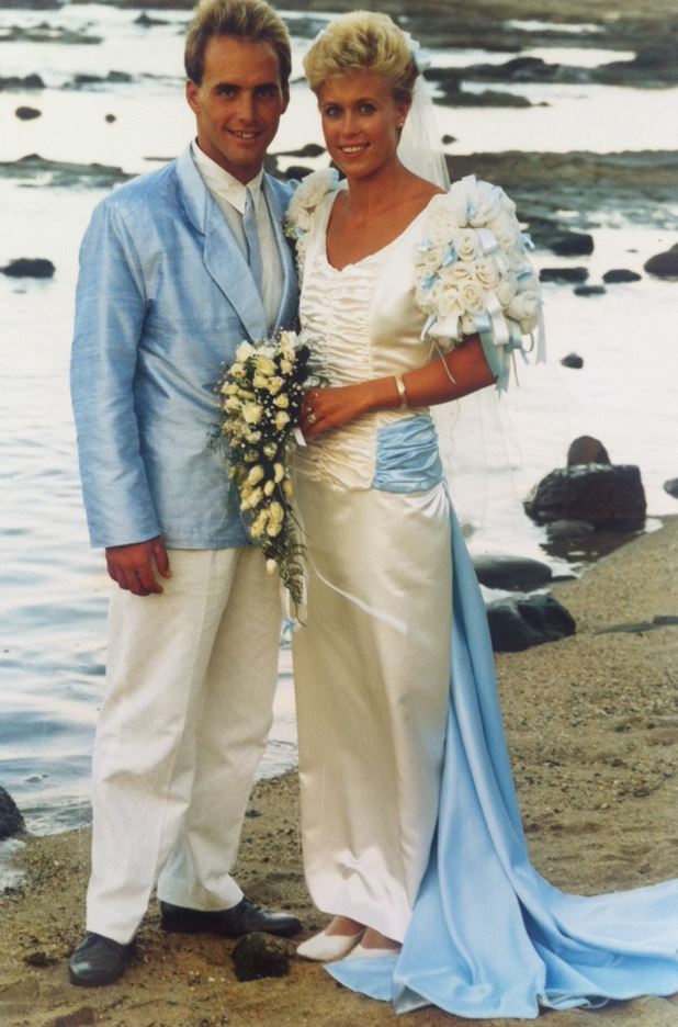 a 1986 photographer of a couple on their wedding day at the beach. Groom wears a shiny blue suit bride flower sleeves on dress