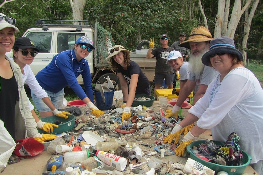 A group of volunteers wearing rubber gloves standing around a table piled with rubbish collected from the ocean