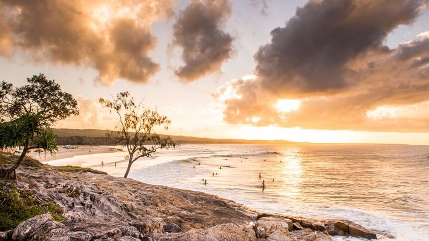 The sunrises over a coastline as people surf.