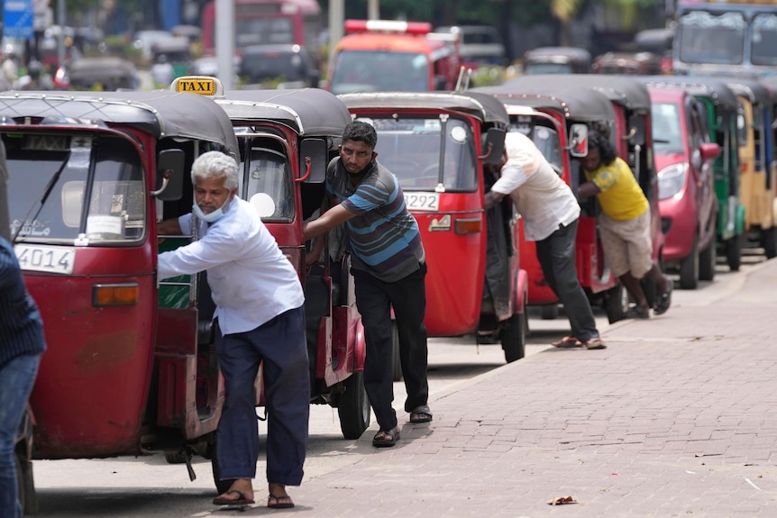Taxi drivers push their auto rickshaw as they wait in a queue to buy petrol.