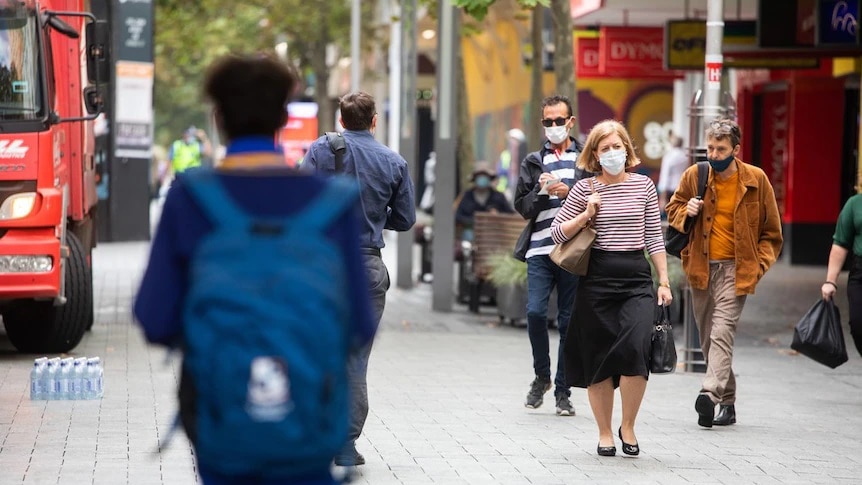 A blurred school child carries their bag while a trio of adults wearing face masks walk by on an inner city street.