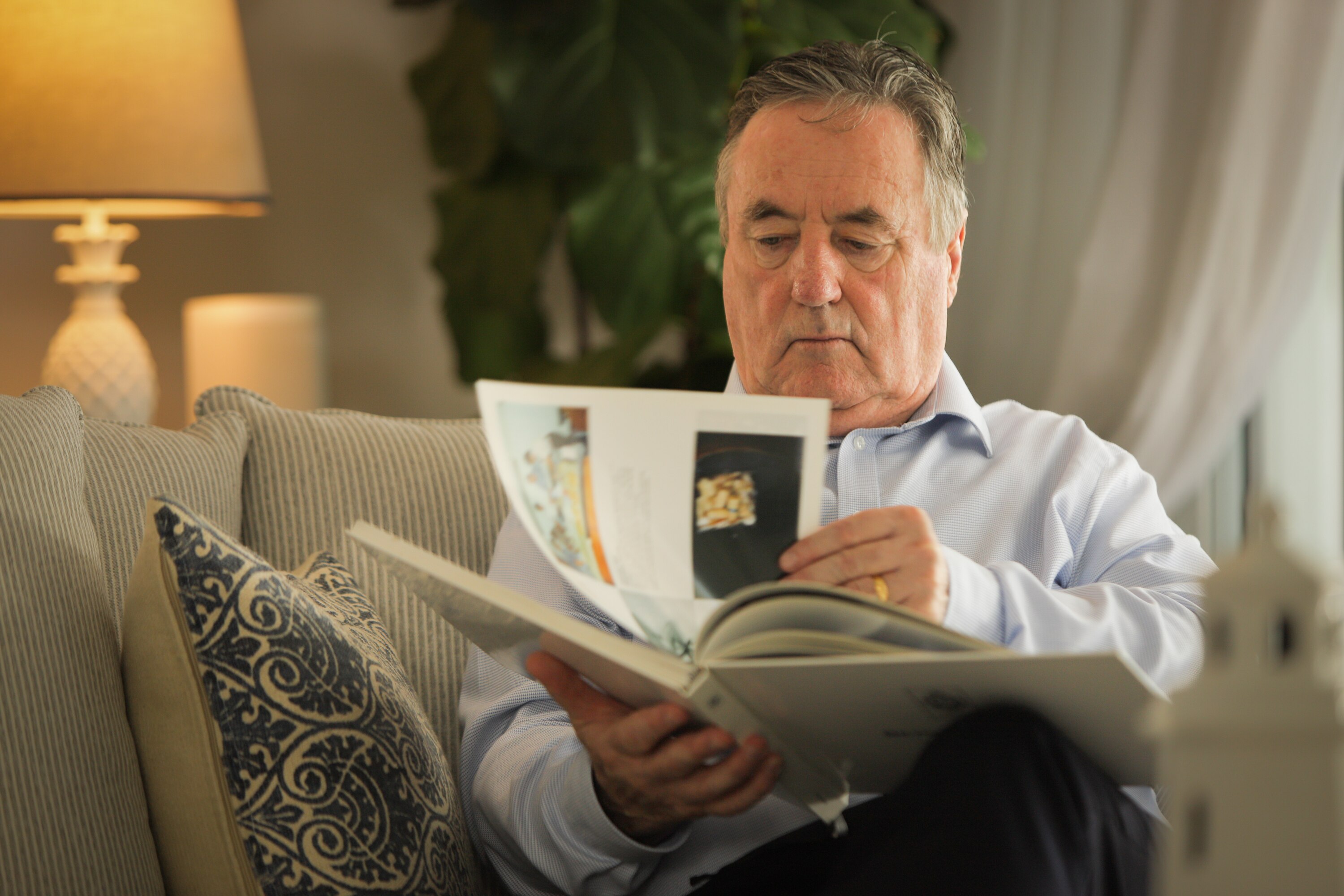 Keelty sits in a couch in a living room leafing through pages of a book.