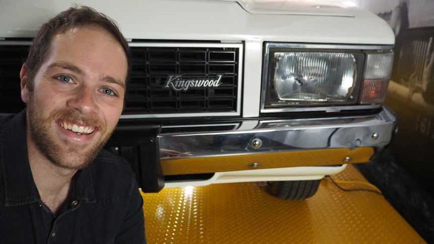 A man crouched in front of an old Holden Kingswood