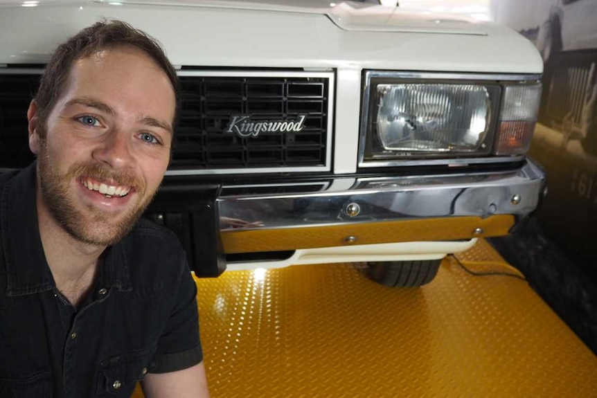 A man crouched in front of an old Holden Kingswood