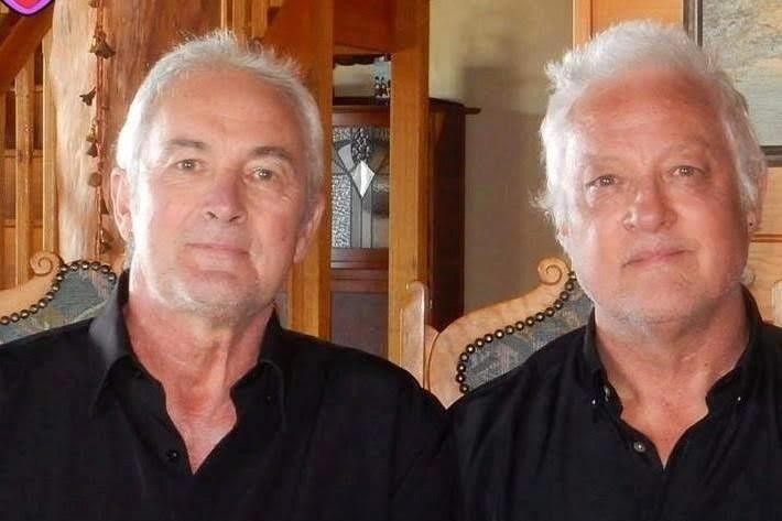 Two men with white hair sitting next to each other on dining chairs
