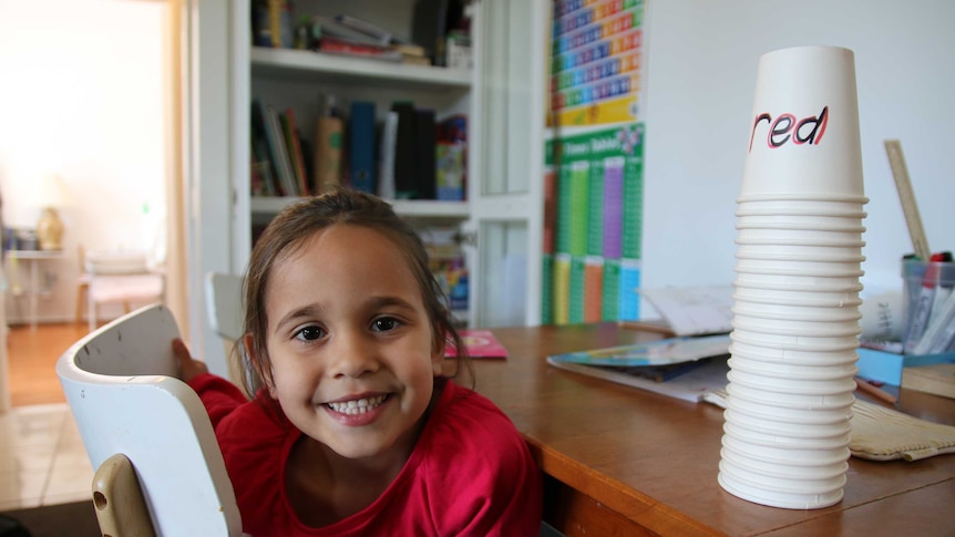 Five-year-old Amity, sits at her desk, smiling into the camera