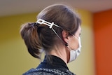 A woman uses a plastic clip behind the head to hold on a surgical face mask