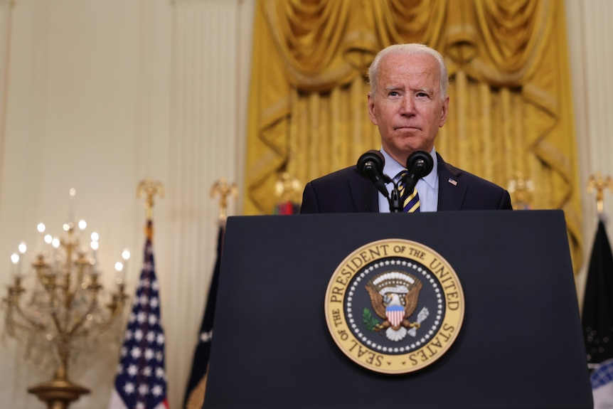 Joe Biden stands behind a lectern with flags behind him. 