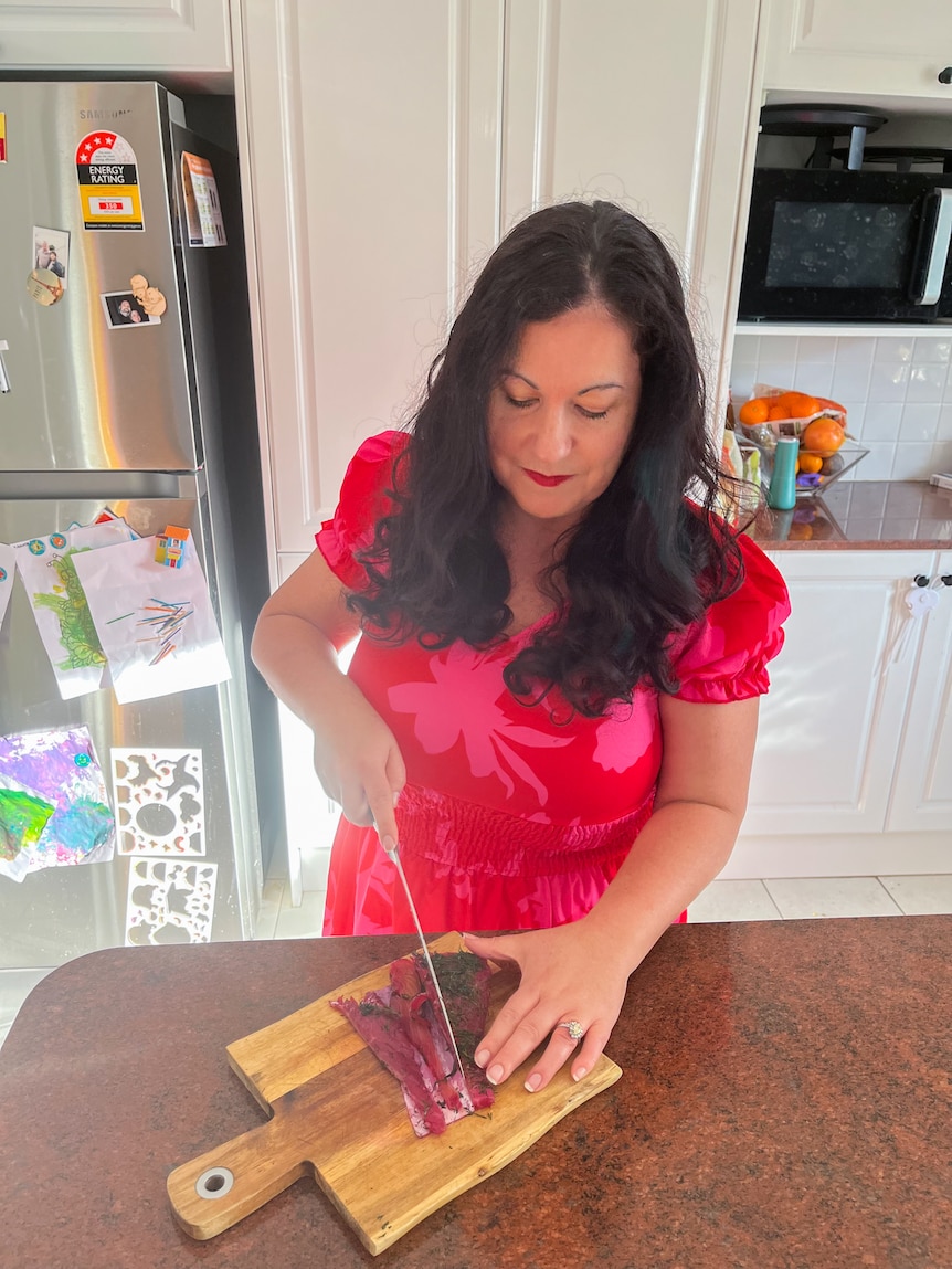 A woman with dark brown hair cuts gravlax into slices on a wooden chopping board in a kitchen.