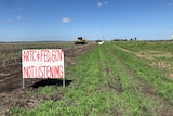 Tractor in field with a sign protesting a 16km inland rail line proposed to be built on floodplain at Millmerran.